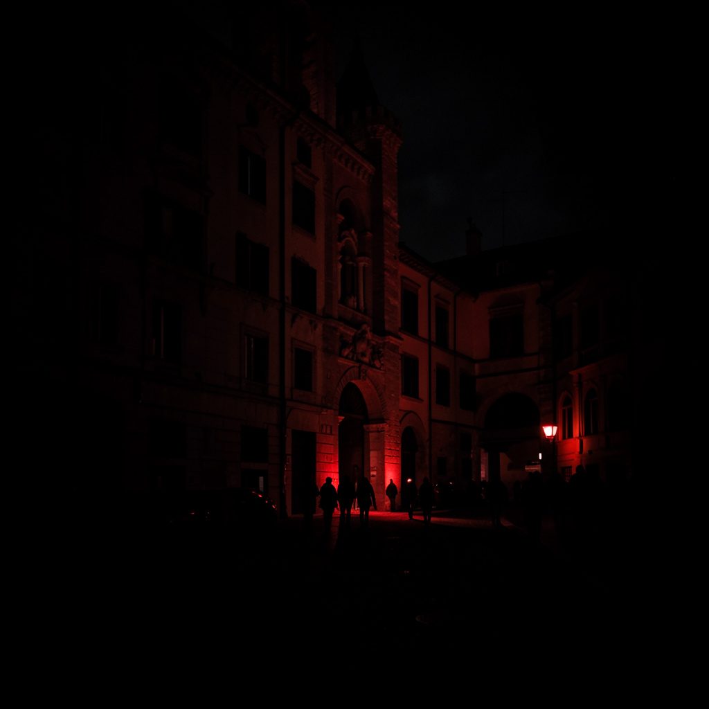 Low-light, high-contrast photograph of a Turin avenue after dusk, dark brick facades and deep shadow